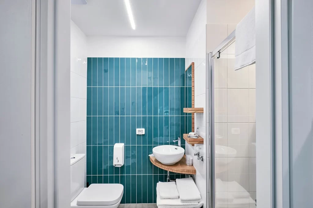 Bagno moderno con piastrelle verdi, lavabo bianco e arredo in legno.