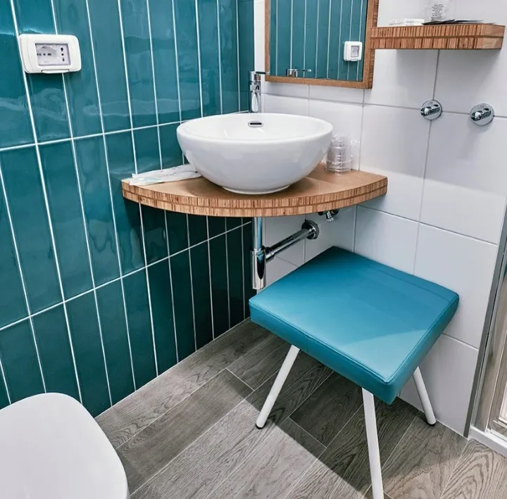 Lavabo bianco con piastrelle verdi e sgabello color turchese in bagno moderno.