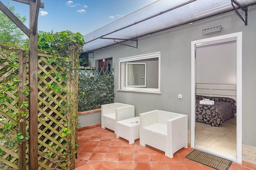 Patio esterno con arredo bianco e piante verdi che offrono privacy.
